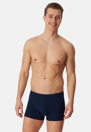 Mørkeblå bomuldsboxershorts med tætsiddende pasform. Har en hvid linning og sømdetaljer. Blød tekstur og midt på låret længde.