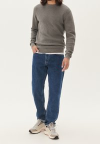 Szary sweter dzianinowy, niebieskie dżinsy oraz jasnoszare trampki. Strój ma casualowy krój z prążkowanymi mankietami i klasycznym wzorem.