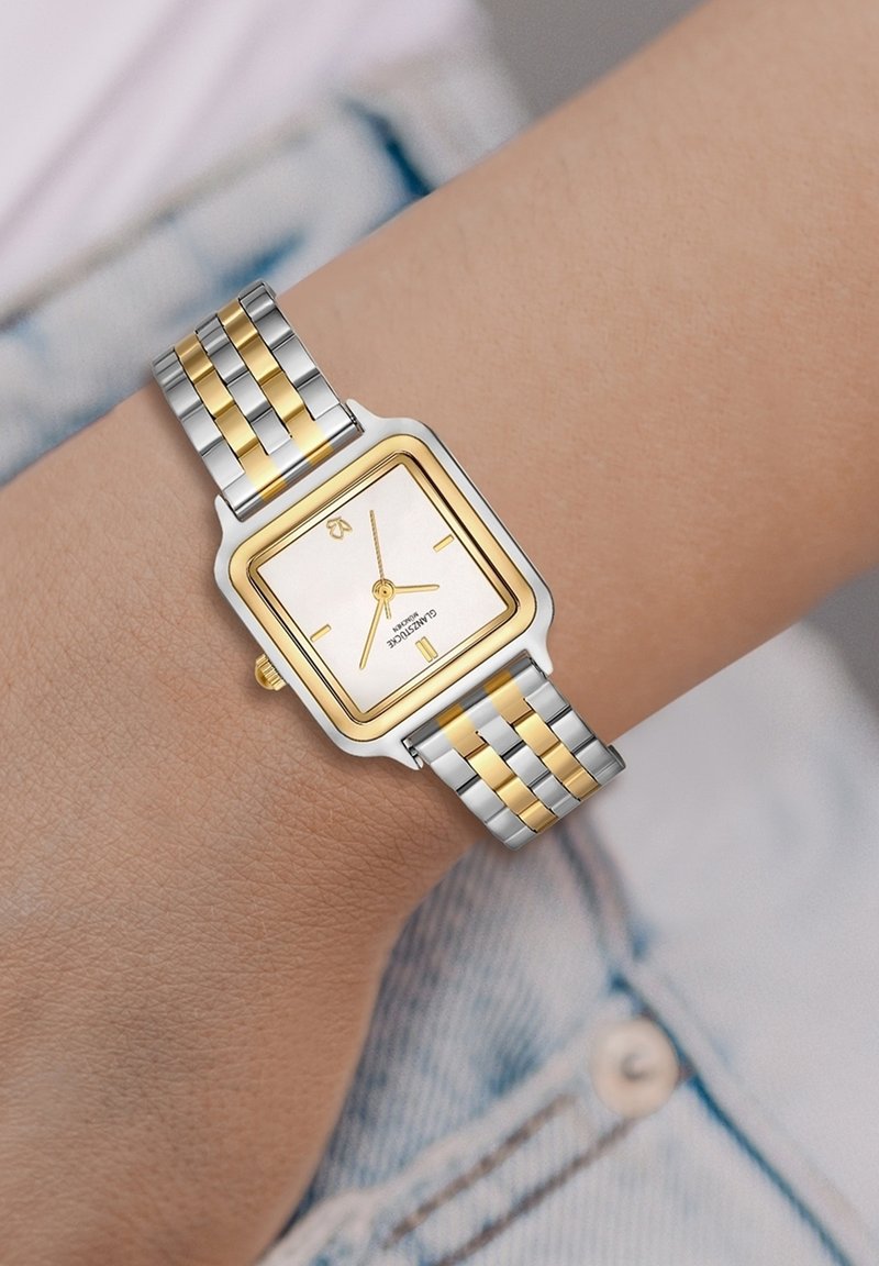 Ruutuline hõbe- ja kuldne kell, valge diali, kuldsete aktsentide ja kahetoonilise metallkettega, kus on ristkülikukujulised lingid.