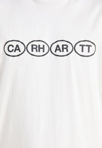 Bijela majica s crnim ovalnim dizajnima na kojima se nalaze slova "CA," "RH," "AR," i "TT" u podebljanom, sans-serif fontu. Mekani pamuk.