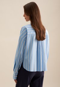 Camicia a maniche lunghe blu a righe con vestibilità ampia, polsini bottonati e design con schiena a spacco. Tessuto liscio e sottili righe bianche.