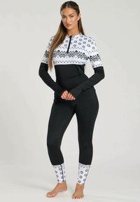 Completo da sci bianco e nero con collezione a zip, caratterizzato da un motivo a fiocchi di neve nella parte superiore e una sezione inferiore completamente nera. Design aderente e elasticizzato.