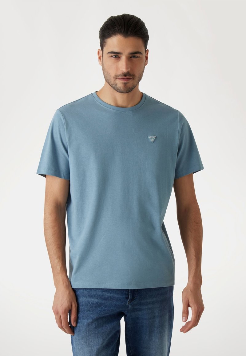 T-shirt in cotone blu con scollo tondo e maniche corte, caratterizzata da un piccolo logo triangolare sul lato sinistro del petto. Tessuto semplice senza fantasie.