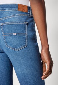Vaqueros de denim azul con un diseño ajustado, que presentan un parche de cuero en la cintura y un pequeño logo bordado en el bolsillo trasero.