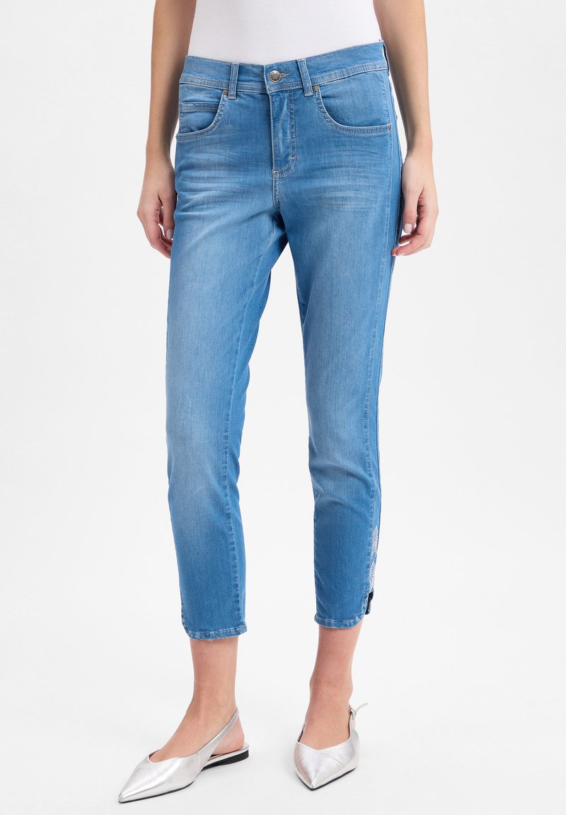 Helle blaue Denim-Jeans mit schlankem Schnitt, knöchelbürtig geschnitten, mit seitlichen Reißverschlüssen und klassischem Fünf-Taschen-Design. Glatte Textur.
