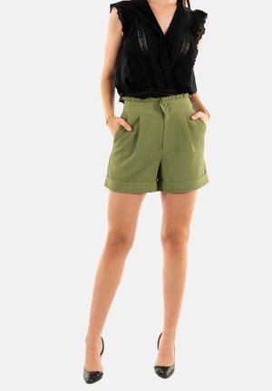 Shorts vert olive avec une surface texturée, taille haute, deux poches latérales et un large revers. Portés avec un haut noir à volants et des talons hauts.