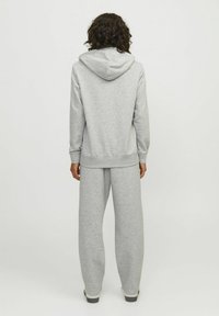 Sudadera de algodón gris con capucha ajustable, combinada con pantalones de chándal holgados a juego. Textura suave, puños acanalados y bajos ajustados.