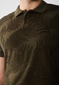 Oliven grønn polo skjorte med teksturert palmebladmønster, med klassisk krage og tre-knapp placket. Mykt stoff med lett glans.