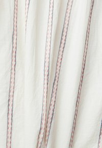 Tissu blanc avec des rayures verticales cousues en rouge et bleu, montrant la texture et des plis doux.