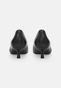 Zwarte leren high heels met een puntige neus en een slanke, gebogen hak. Heeft stiksels langs de bovenkant.