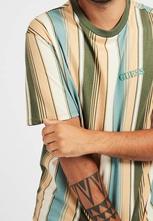 T-shirt en coton rayé présentant des lignes verticales vertes, beiges et bleues. Contient le logo "GUESS" brodé sur la poitrine.