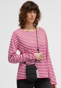 Red and white striped long-sleeve shirt with a round neckline, paired with a small black quilted crossbody bag featuring a label.