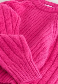 Ružový pletený sveter s rebrovanou textúrou, dlhými rukávmi a okrúhlym výstrihom. Tkanina vyzerá mäkko a nadýchane.