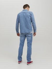 Chaqueta de mezclilla azul claro con cuello y puños abotonados, combinada con jeans azul claro a juego. Zapatillas rojas añaden un contraste de color.
