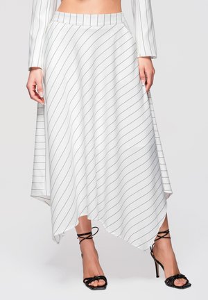 Jupe asymétrique blanche avec de fines rayures diagonales noires portée avec des sandales à talons aiguilles noires à brides sur un mannequin.