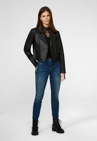 Svart läderkortjacka med asymmetrisk dragkedja, tillsammans med medelblå skinny jeans och svarta snörkängor.
