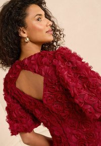 Red floral-embellished dress with puffed sleeves; features a keyhole back and layered rose patterns in lightweight fabric.