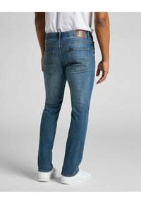 Jean en denim bleu à coupe slim, avec une étiquette en cuir de la marque Lee, des poches arrière et un léger effet délavé sur tout le tissu.