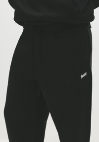 Black jogger pants made of soft fabric, featuring an elastic waistband with drawstring and a small white logo on the lower leg.