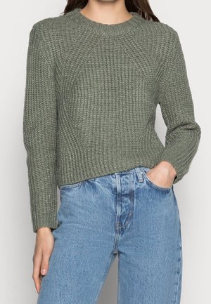Maglione verde a costine con scollo rotondo e maniche lunghe, abbinato a jeans azzurri a vita alta con vestibilità rilassata.