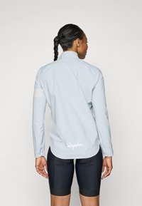 Light blue cycling jacket with a high collar, long sleeves, elastic cuffs, and a logo at the back. Smooth, lightweight fabric.