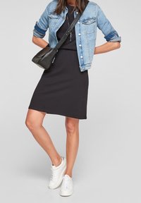 Vestido negro de jersey con forma ajustada, combinado con una chaqueta de denim azul claro y un bolso cruzado negro. Zapatillas blancas completan el look.