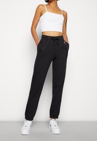 Svarta träningbyxor med elastisk midja och dragsko, med sidfickor och kontrasterande sömmar. Kallas med en vit croptop och sneakers.