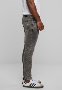 Vaqueros de mezclilla gris ajustados con textura desvaída, cinco bolsillos y cinturilla negra, combinados con zapatillas blancas con acentos en negro y gris.