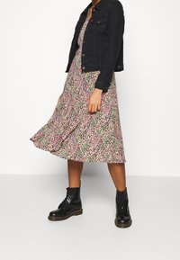 Schwarze Jeansjacke über einem fließenden Midikleid mit pinken und grünen Blumen, kombiniert mit schwarzen Schnürstiefeletten.