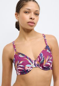 Μωβ φλοράλ πάνω μέρος μπικίνι με βαθιά τριγων ική σχεδίαση, ρυθμιζόμενες τιράντες και σούρες στο κέντρο για επιπλέον λεπτομέρεια.