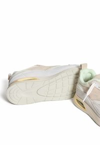 Sport sneakers in lichtbeige en wit, met een gestructureerde suède bovenkant, een gevoerde hiel met zichtbare luchtunit en een flexibele rubberen zool.