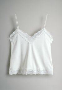 Balts kamzolis ar regulējamām plānām lencītēm, izrotāts ar smalku mežģīņu apdari pie izgriezuma un apakšmalas. Vienmērīga auduma tekstūra.