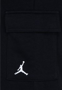 Czarna bawełniana kieszeń z białym logo Jumpman. Kieszeń ma prostokątną klapkę z przeszytymi brzegami i gładką fakturą.