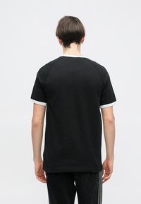 Čierne tričko s krátkym rukávom a bielymi akcentmi na výstrihu a rukávoch, s voľným strihom a jemnou textúrou. Zobrazený zadný pohľad.
