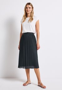 Black pleated midi skirt with a textured finish and elastic waistband, paired with a white short-sleeve top and silver strappy sandals.