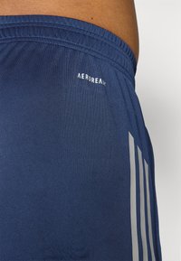 Tummansiniset shortsit, jotka on valmistettu pehmeästä kankaasta, sisältävät elastisen vyötärönauhan, pienen "AEROREADY"-logon ja kolme harmaata viistosti sivuilla.
