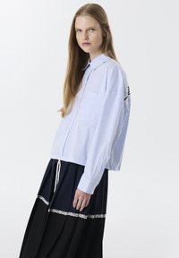 Camisa a rayas azul y blanca con diseño de botones, que incluye un bolsillo en el pecho y mangas largas. Combinada con una falda en tonos navy y negro con bordes de encaje.