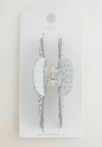 Glitzernder silberner Haarklammer mit Strassakzenten, die einen zentralen Federmechanismus und eine Sanduhrform aufweist, montiert auf einer weißen Karte.