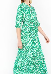 Grön och vit midiklänning med leopardmönster, V-ringning och midja med bälte, puffärmar och en svävande kjol.