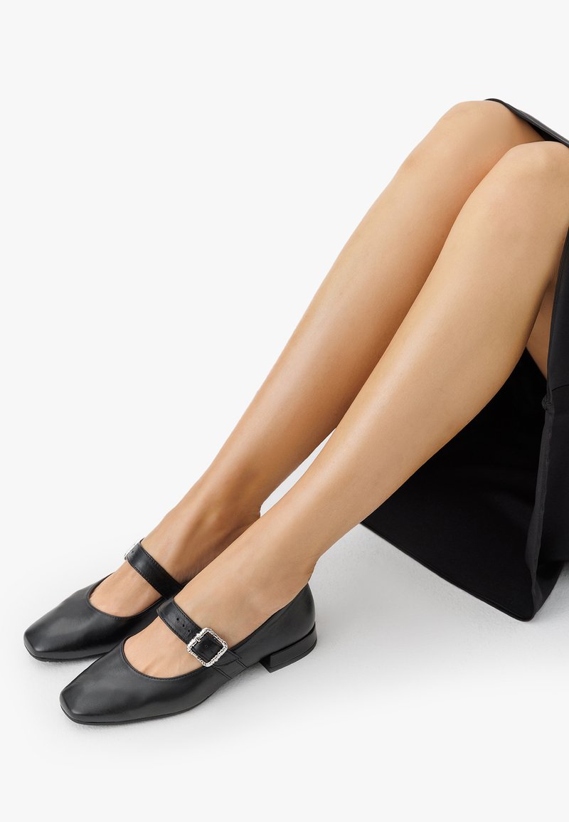 Zapatos Mary Jane de cuero negro con punta cuadrada, un pequeño tacón cuadrado y una hebilla decorativa en la correa. Textura suave, diseño minimalista.