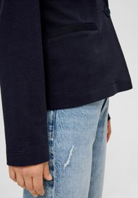 Granatowa bawełniana kurtka o dopasowanym kroju, z pojedynczym zapięciem na guzik, eleganckimi liniami i kieszenią po lewej stronie.