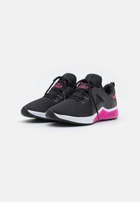 Zapatillas deportivas negras con parte superior texturizada, detalles en rosa en la suela y la marca, y una media suela blanca con una unidad de aire visible.