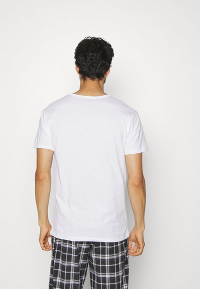Camiseta de algodón blanca con mangas cortas, cuello redondo y corte relajado. Combinada con pantalones de pijama a cuadros en azul marino y blanco.