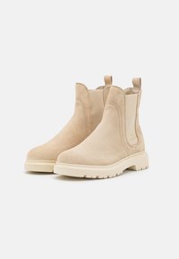 Bottines en daim beige avec des panneaux latéraux élastiques et des languettes de tirage. Semelles en caoutchouc chunky beige clair avec une semelle texturée pour une meilleure adhérence.