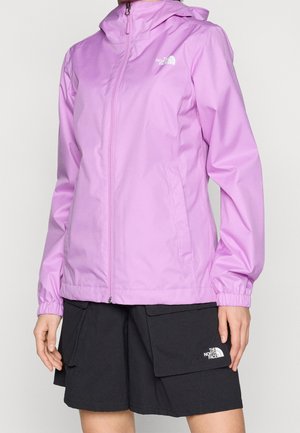 Woman wearing light purple hooded zip-up jacket and black cargo shorts, both branded The North Face, standing against a plain background.