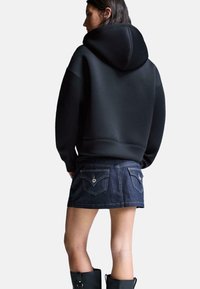 Zwarte hoodie met een gladde stof, gecombineerd met een donkere spijkerrok met achterzakken en contrasterende gele stiksels.