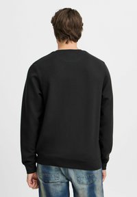 Zwarte crewneck sweatshirt van zacht materiaal, met lange mouwen en een geribbelde zoom, gecombineerd met lichtblauwe distressed jeans.