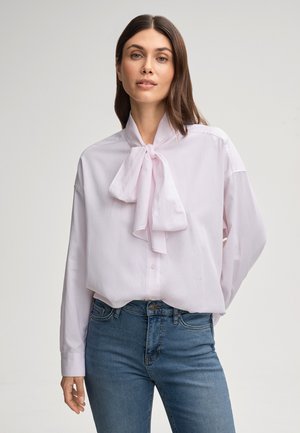 Lichtroze blouse met een strikcol, lange mouwen en knopen aan de voorkant. Soepele textuur. Gecombineerd met blauwe denim jeans.