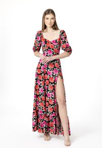 Robe longue noire à fleurs avec des roses roses et rouges, manches bouffantes et une fente haute sur la cuisse ; ourlet festonné en bas. Talons transparents.