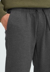 Ciemnoszare dresy z teksturowanej tkaniny, z elastycznym paskiem w talii i sznurkiem, z bocznymi kieszeniami oraz luźnym krojem.